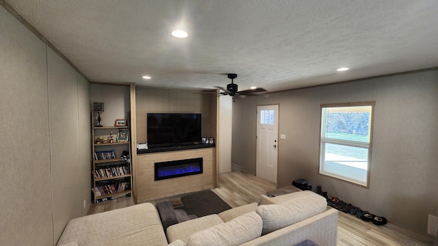 living area featuring a textured ceiling, light wood-style flooring, recessed lighting, a large fireplace, and a ceiling fan