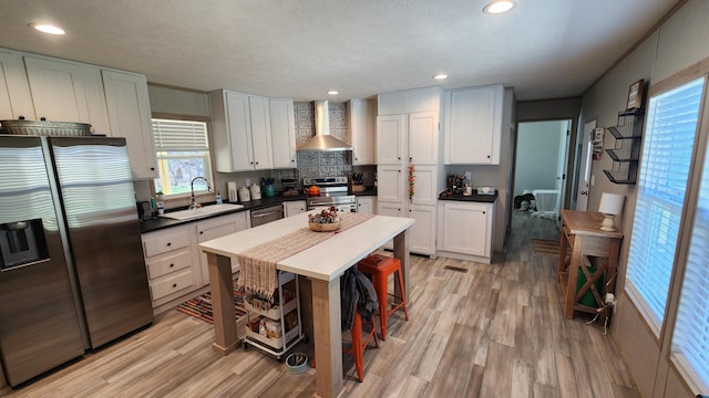 kitchen with stainless steel appliances, light wood-type flooring, a sink, and wall chimney range hood