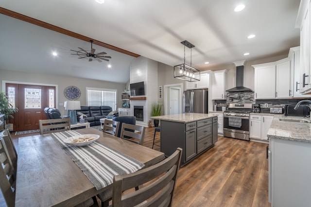 kitchen featuring white cabinets, appliances with stainless steel finishes, open floor plan, wall chimney range hood, and a sink