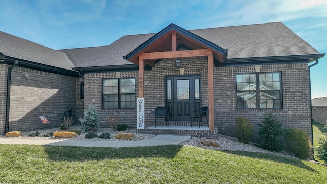 view of front of home with covered porch, brick siding, a shingled roof, and a front yard