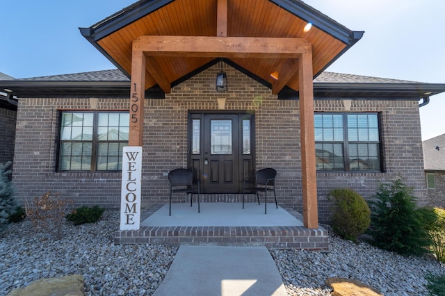 property entrance featuring covered porch, brick siding, and a shingled roof