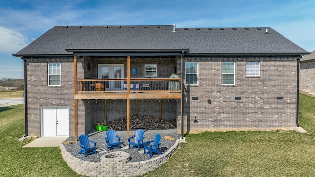 back of house with an outdoor fire pit, a shingled roof, a lawn, and brick siding