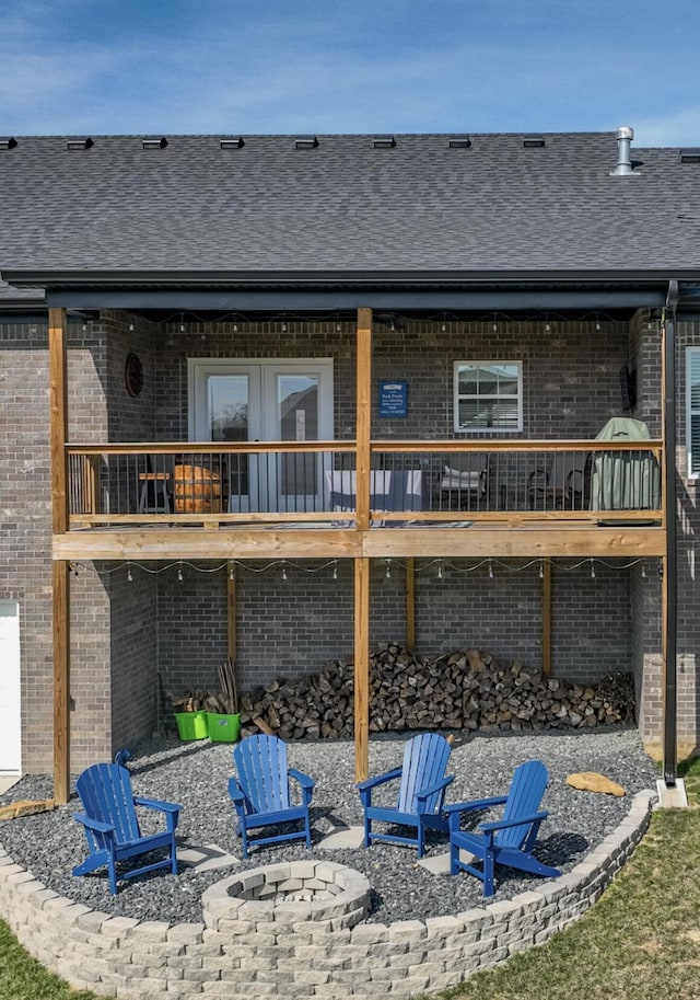 back of house featuring a fire pit, brick siding, and roof with shingles