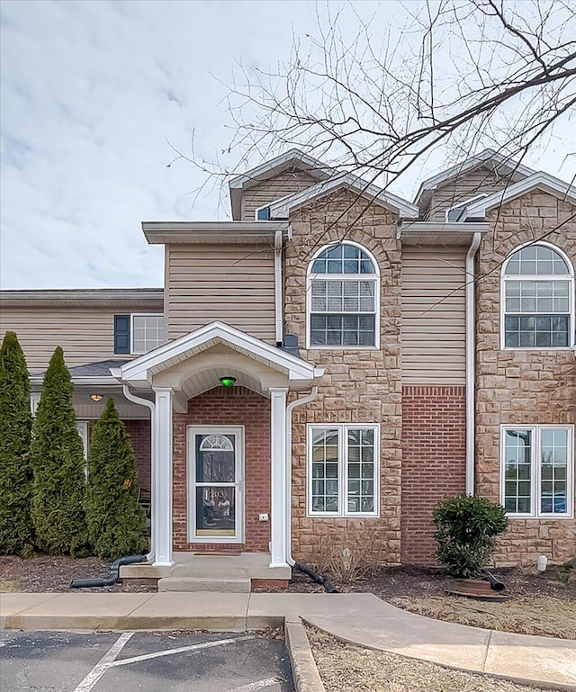 view of front facade featuring uncovered parking, stone siding, and brick siding