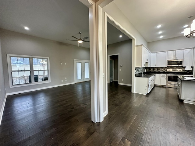 kitchen with stainless steel appliances, dark countertops, dark wood-type flooring, open floor plan, and a sink