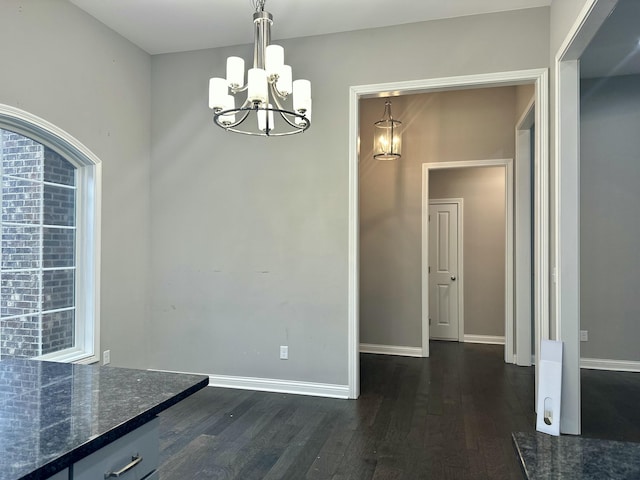 unfurnished dining area with dark wood finished floors, baseboards, and an inviting chandelier