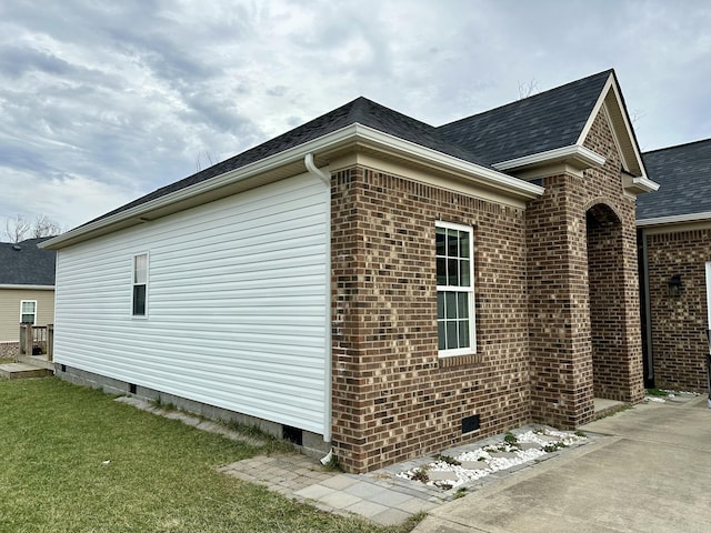 view of side of home with crawl space, brick siding, a lawn, and a shingled roof