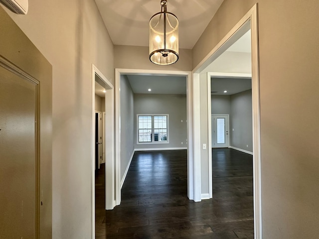 corridor with a chandelier, dark wood-style flooring, a wall mounted AC, and baseboards