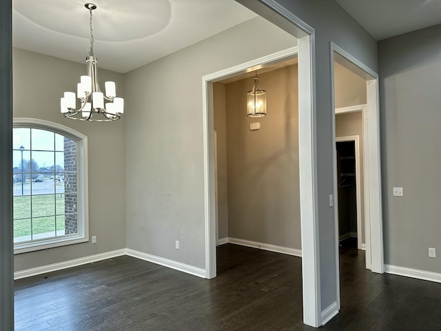 unfurnished dining area with dark wood-type flooring, a notable chandelier, and baseboards