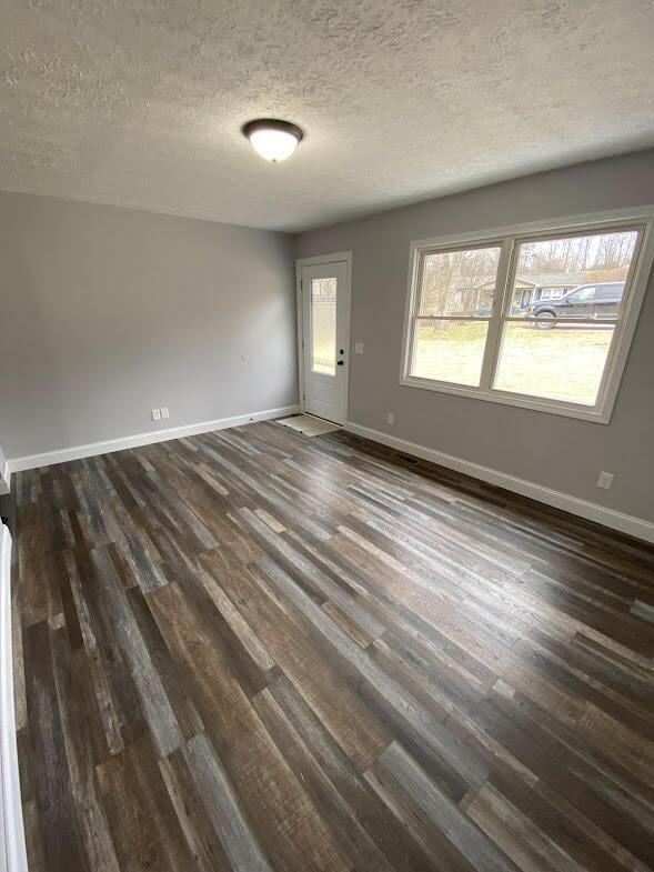 empty room featuring a textured ceiling, baseboards, and dark wood-type flooring