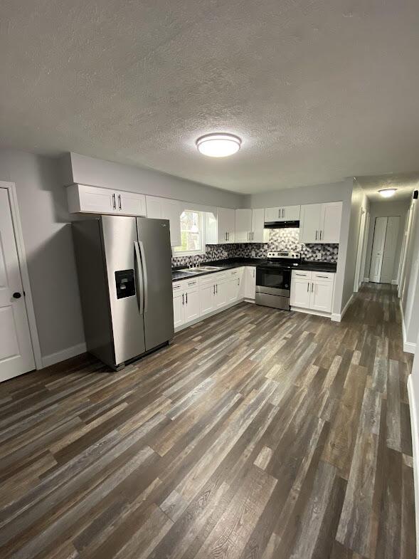 kitchen featuring dark countertops, dark wood-type flooring, stainless steel appliances, and decorative backsplash