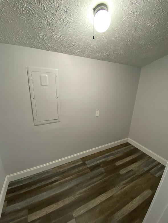 empty room featuring dark wood-type flooring, electric panel, a textured ceiling, and baseboards