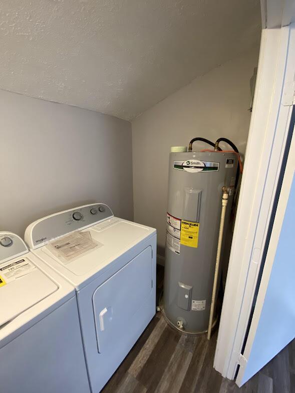 clothes washing area featuring dark wood-style floors, washing machine and clothes dryer, water heater, a textured ceiling, and laundry area