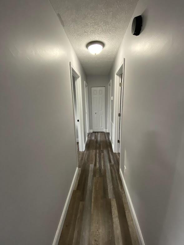 hall with a textured ceiling, dark wood-type flooring, and baseboards