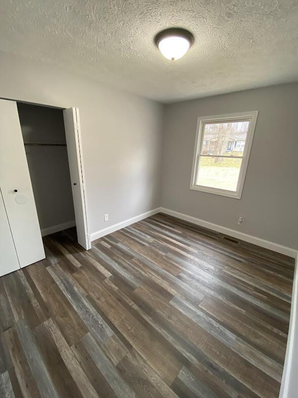 unfurnished bedroom with dark wood finished floors, a closet, visible vents, a textured ceiling, and baseboards