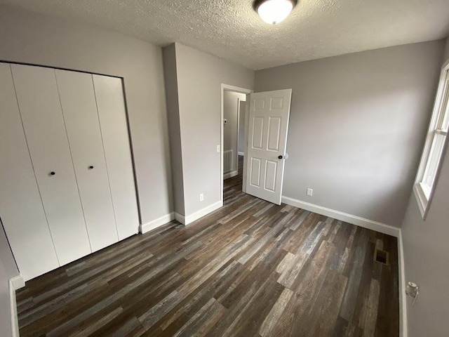 unfurnished bedroom featuring baseboards, visible vents, dark wood-style flooring, a textured ceiling, and a closet