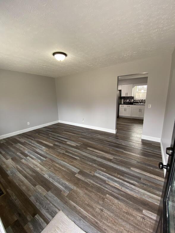 empty room featuring baseboards, dark wood finished floors, and a textured ceiling