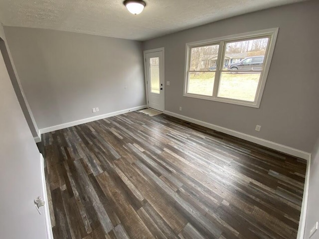 spare room featuring a textured ceiling, baseboards, and dark wood-style flooring