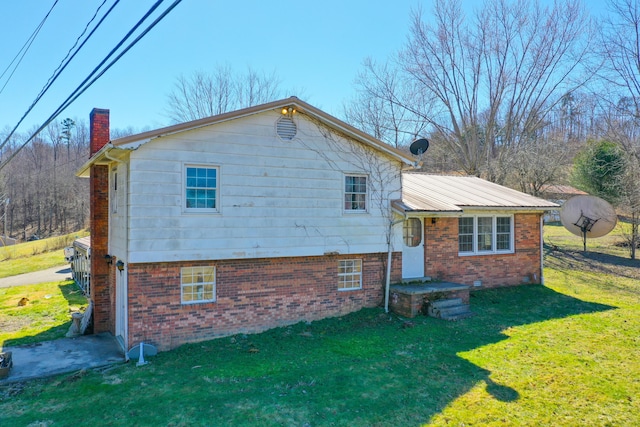 view of front facade with brick siding, metal roof, a chimney, and a front lawn