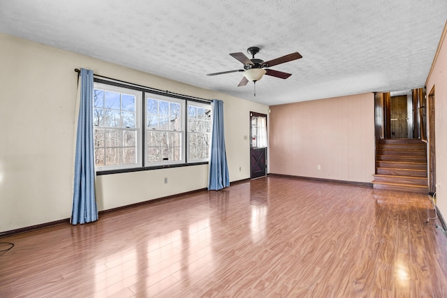 unfurnished room with a textured ceiling, wood finished floors, a ceiling fan, baseboards, and stairway