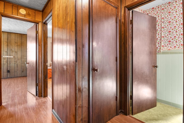 hallway featuring a textured ceiling, wood finished floors, and wooden walls