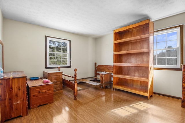 bedroom featuring light wood-type flooring, baseboards, and a textured ceiling