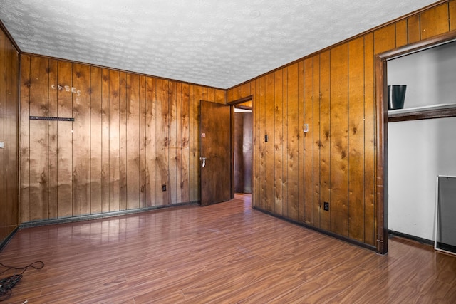 spare room featuring wood walls, a textured ceiling, baseboards, and wood finished floors