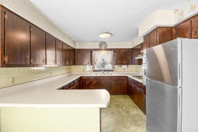 kitchen with decorative backsplash, electric cooktop, freestanding refrigerator, a peninsula, and a sink