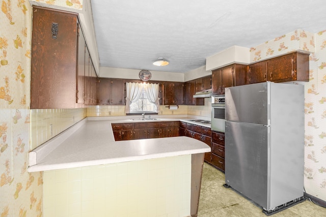 kitchen featuring oven, wallpapered walls, under cabinet range hood, and freestanding refrigerator