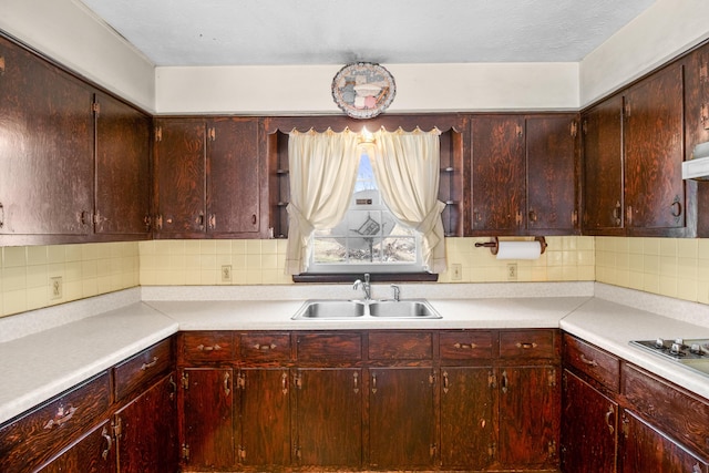 kitchen with light countertops, stainless steel stovetop, a sink, and decorative backsplash