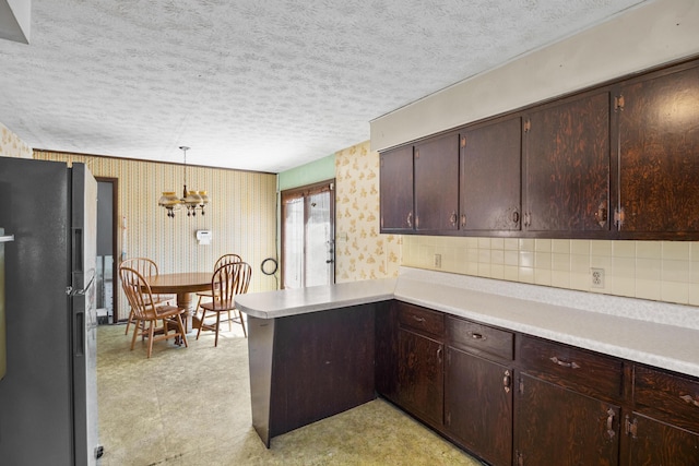 kitchen featuring light floors, light countertops, freestanding refrigerator, a peninsula, and wallpapered walls