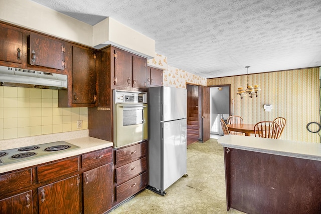 kitchen with under cabinet range hood, electric cooktop, white oven, freestanding refrigerator, and wallpapered walls