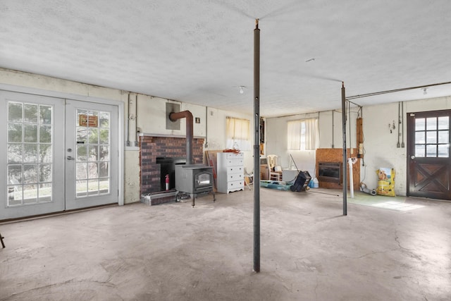 basement with a wood stove, heating unit, a textured ceiling, and french doors