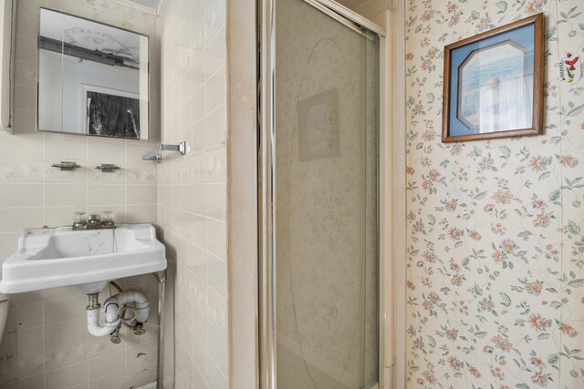 full bath with a sink, wallpapered walls, a shower stall, and tile walls