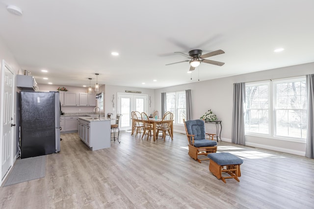 kitchen with a sink, light wood-style floors, gray cabinets, freestanding refrigerator, and a kitchen bar