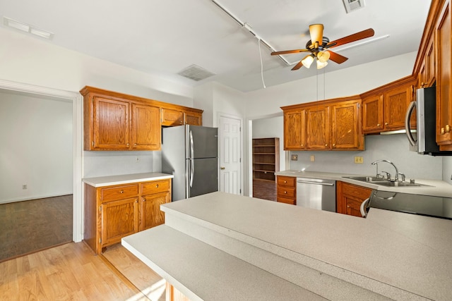 kitchen featuring light countertops, appliances with stainless steel finishes, light wood-style floors, a sink, and a peninsula