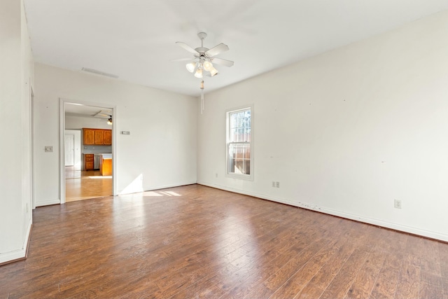 empty room with visible vents, wood-type flooring, a ceiling fan, and baseboards