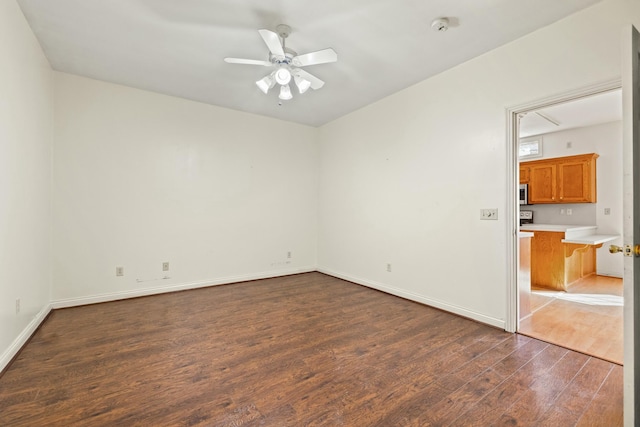 empty room featuring ceiling fan, baseboards, and dark wood finished floors