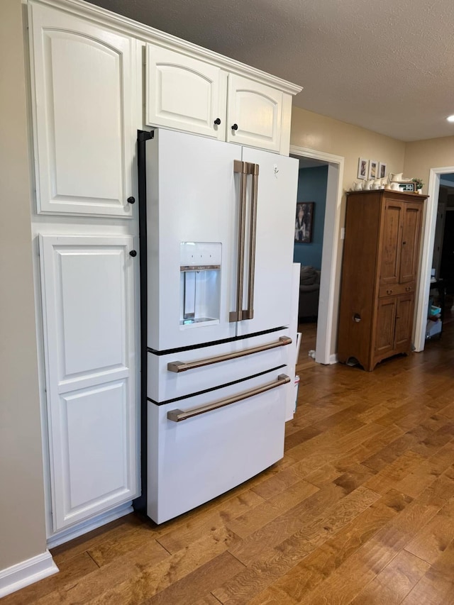 kitchen featuring a textured ceiling, white fridge with ice dispenser, light wood-type flooring, and white cabinets