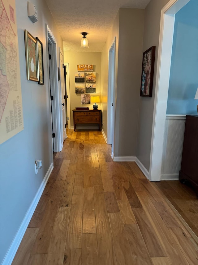 corridor with baseboards, a textured ceiling, and hardwood / wood-style floors