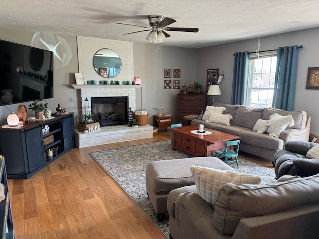 living area with a brick fireplace, ceiling fan, light wood-style flooring, and a textured ceiling