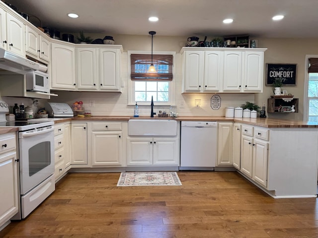 kitchen with light wood-style floors, a sink, a peninsula, white appliances, and under cabinet range hood