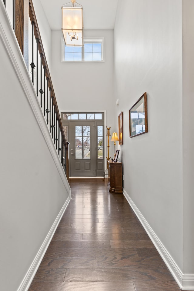 foyer featuring a notable chandelier, dark wood-type flooring, a towering ceiling, baseboards, and stairway