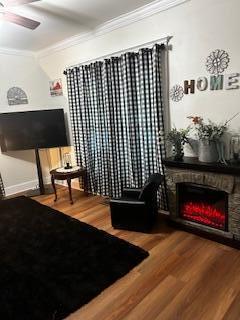 living area with ceiling fan, ornamental molding, wood finished floors, and a stone fireplace