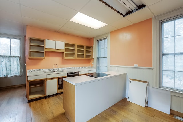 kitchen with a peninsula, a sink, black appliances, open shelves, and light wood finished floors