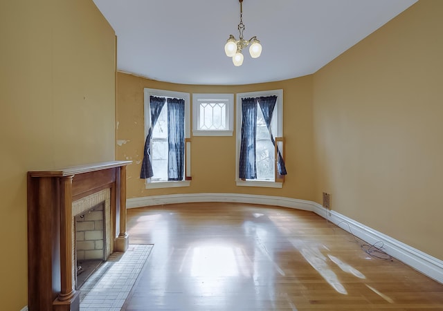 unfurnished dining area with a brick fireplace, baseboards, wood finished floors, and an inviting chandelier