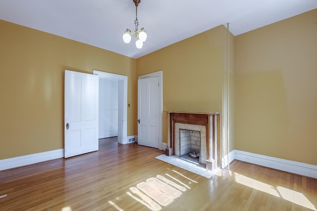 unfurnished living room with a notable chandelier, wood finished floors, visible vents, baseboards, and a tiled fireplace