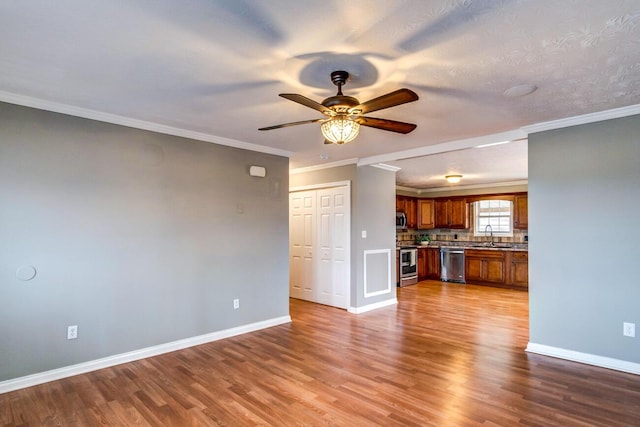 unfurnished living room with ornamental molding, wood finished floors, and baseboards