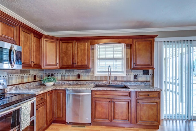 kitchen featuring light stone counters, decorative backsplash, appliances with stainless steel finishes, brown cabinetry, and a sink