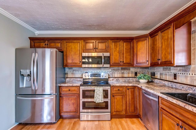 kitchen featuring light wood finished floors, tasteful backsplash, appliances with stainless steel finishes, and brown cabinets